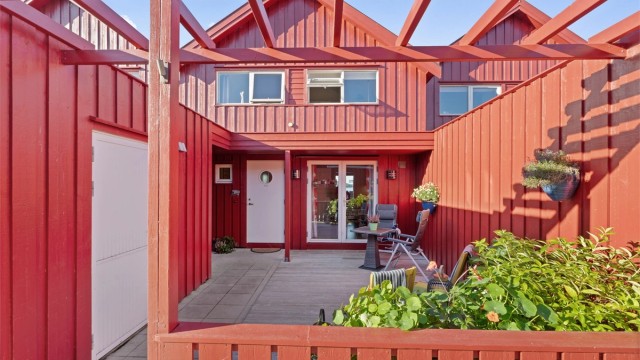 Skjermet terrasse belagt med terrassebord og betongheller ved inngangen.