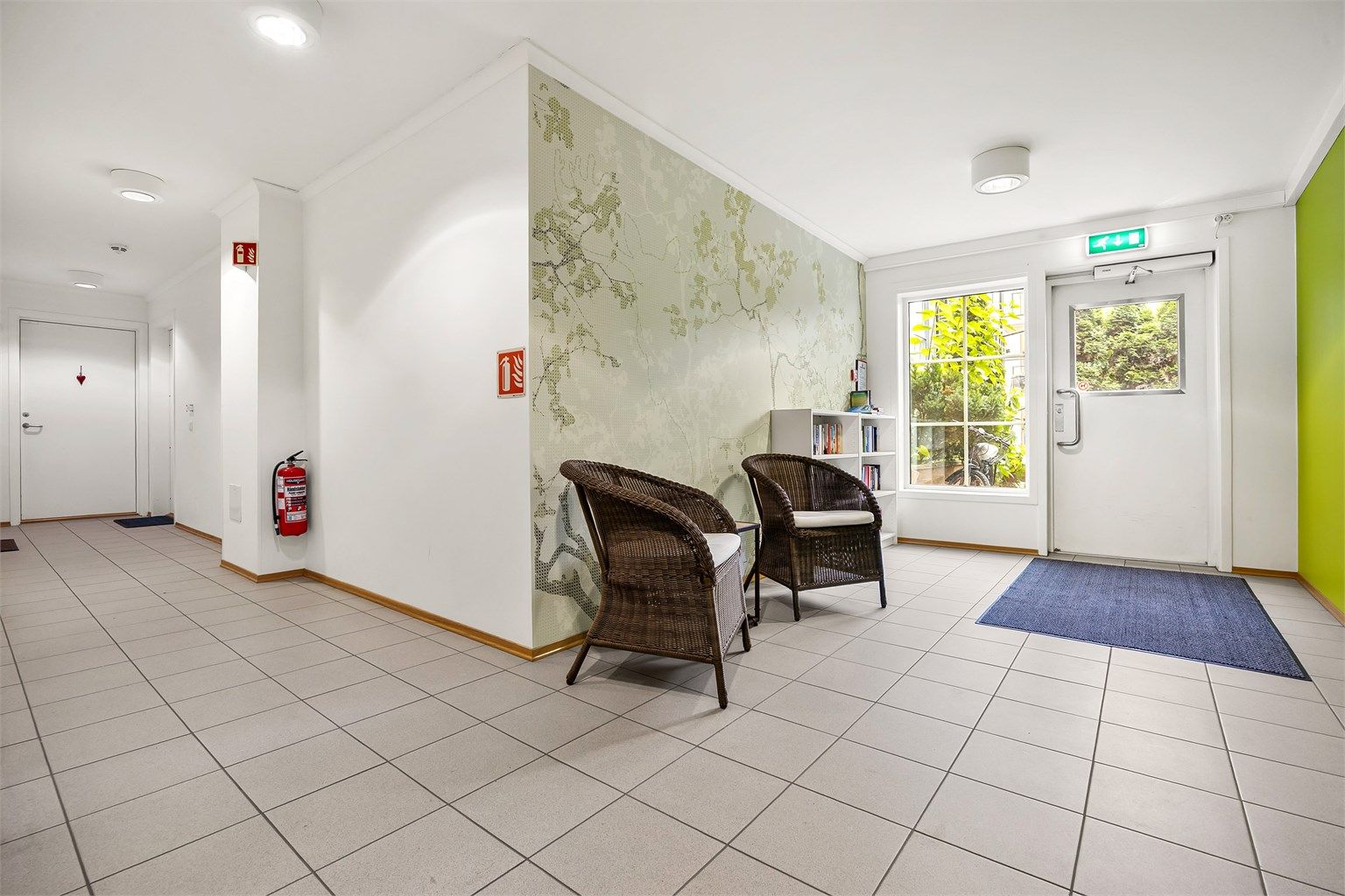 Felles inngangsparti med sittegruppe, bokhjørne og heis til etasjene.