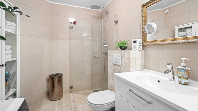 Flislagt bad med varmekabler i gulv. Rommet er utstyrt med vegghengt toalett tilkoblet innebygget sisterne og vegghengt servantskap med ovenpåliggende vask. Videre er det nedsenket dusjsone med innfellbare dusjdører og armatur tilkoblet hånd- og regndusj.