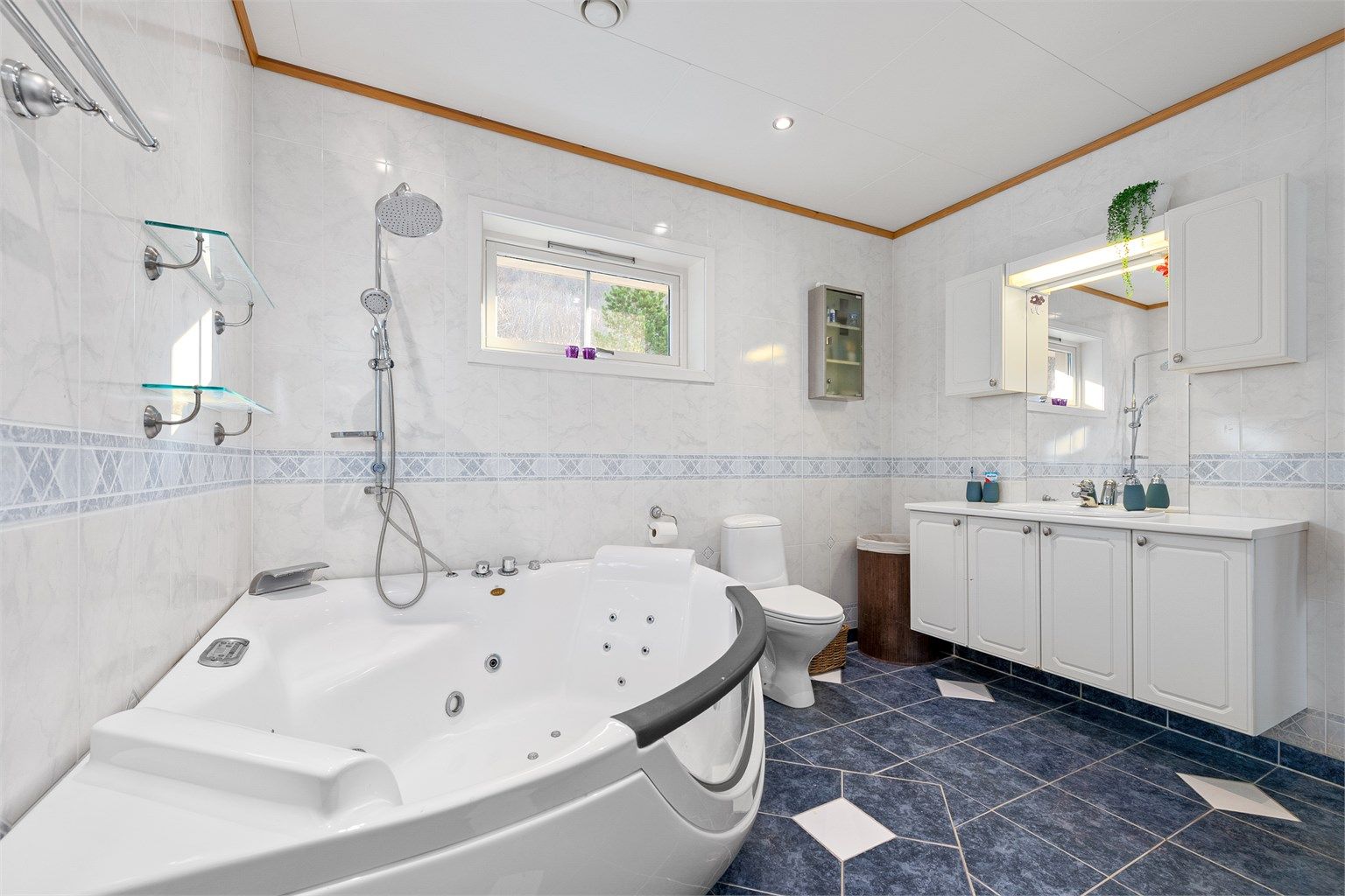 Badet har stor baderomsinnredning med profilerte fronter og ovenpåliggende servant. Speil og skal over servant. Gulvstående toalett.