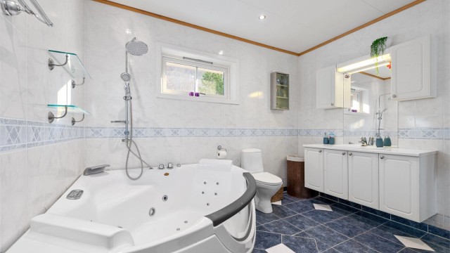 Badet har stor baderomsinnredning med profilerte fronter og ovenpåliggende servant. Speil og skal over servant. Gulvstående toalett.