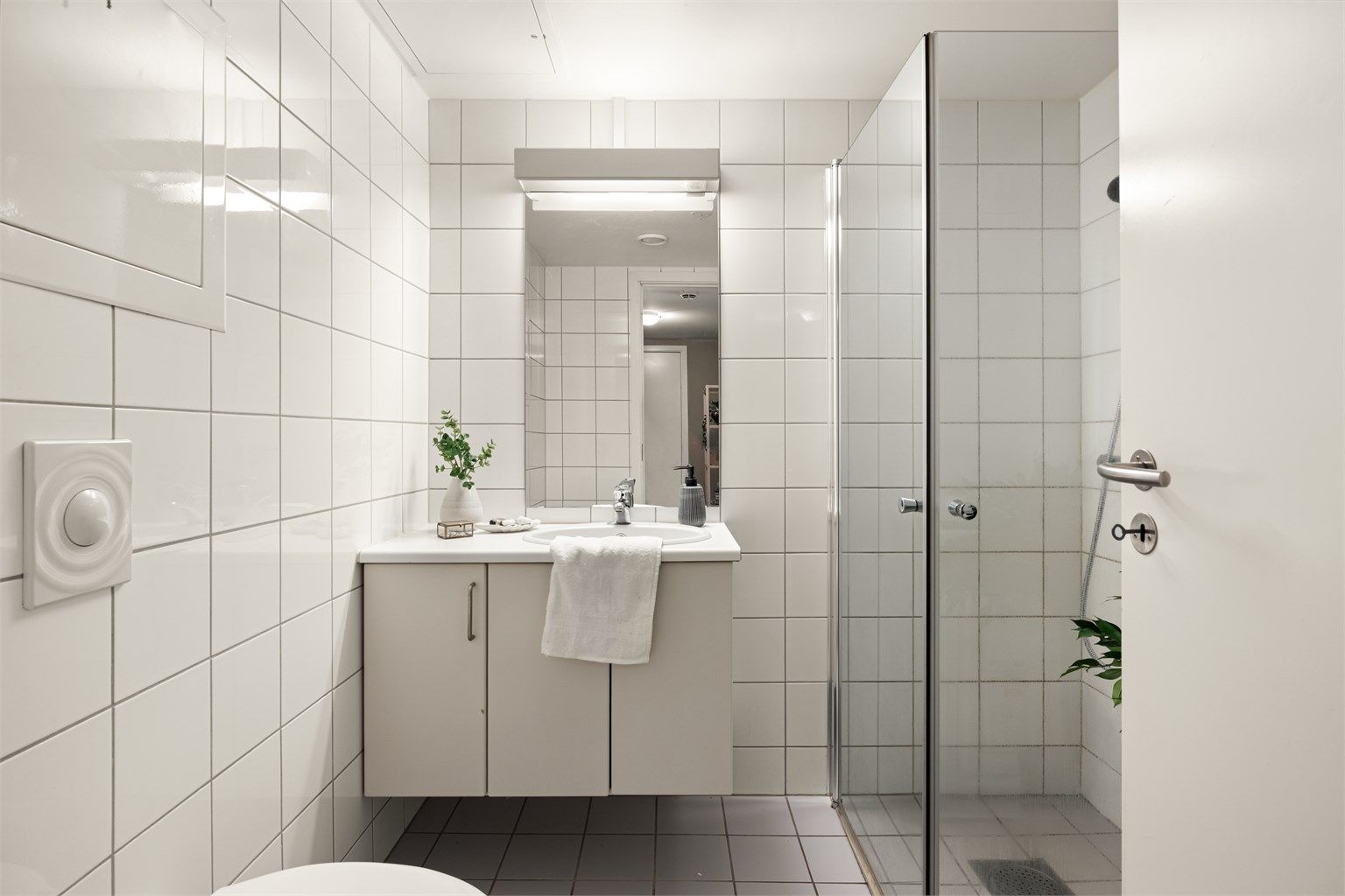 Badet er utstyrt med vegghengt toalett, servant med underskap og dusjhjørne med innfellbare glassdører.