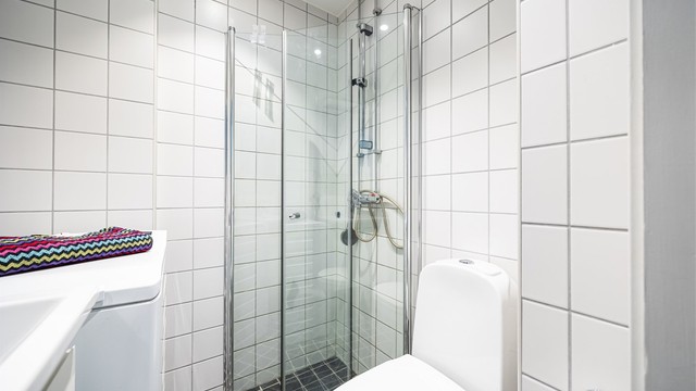 Videre er det gulvstående toalettt og egen dusjsone med innfellbare glassdører.