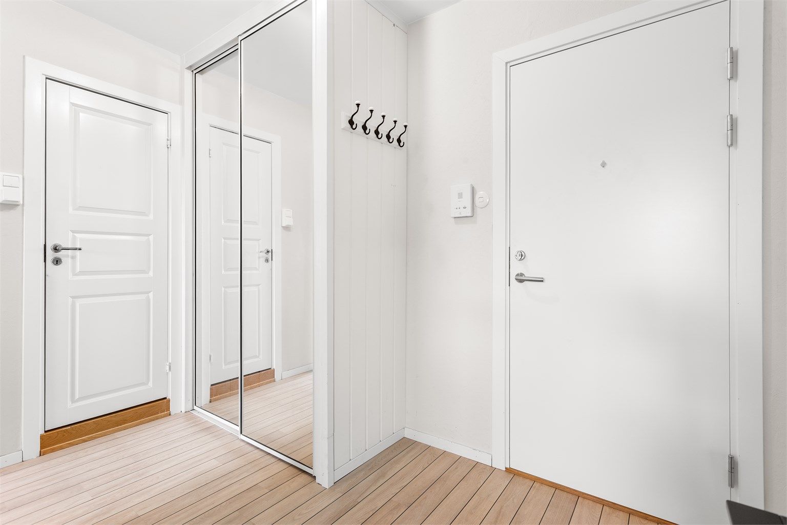 Dørcallinganlegg med åpnerfunksjon og skyvedørsgarderobe med speilfronter i entré.