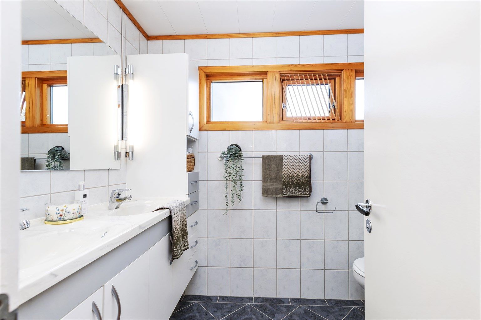 Badet i 1. etasje ble oppgradert i 2001 og er innredet med flislagte gulv og vegger, gulvvarme, dusjhjørne, vegghengt toalett og servantinnredning.