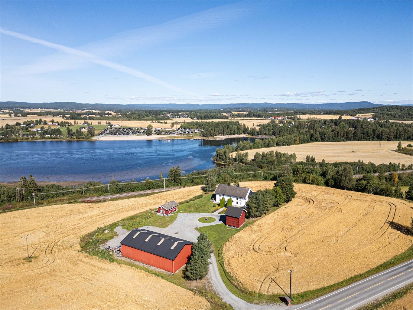 Sommerlig oversikt over eiendommen med omkringliggende jorder og vann.
