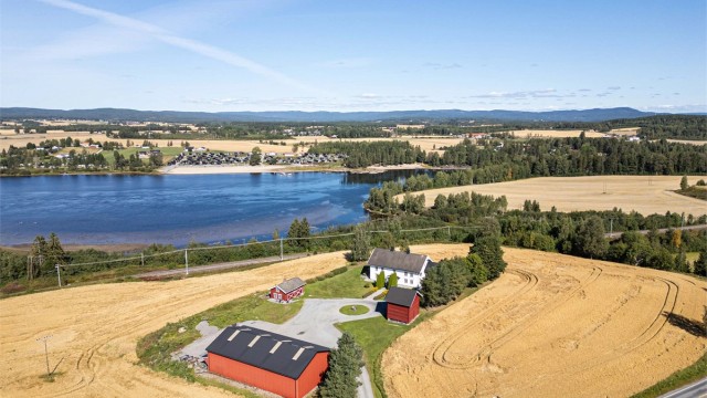 Sommerlig oversikt over eiendommen med omkringliggende jorder og vann.