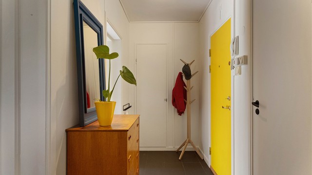 Entréen tar imot deg med mørke gulvfliser, en solgul dør og fargerike detaljer som gir et varmt og personlig førsteinntrykk. Her er det god plass til yttertøy, sko og oppbevaringsmøbler.