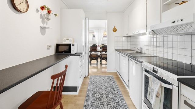 Kjøkkeninnredning med glatte fronter, laminatbenkeplate og fliser over benken.