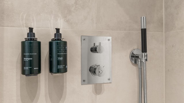 usjnisje med glassvegg og integrert dusjarmatur i vegg og med integrerte rør i vegg til hånddusj og regnfallsdusj