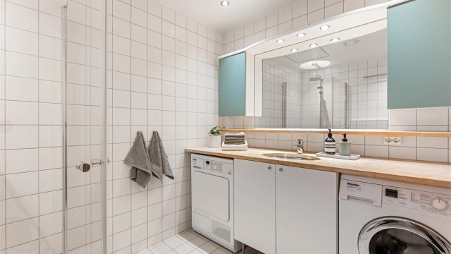 Servantskap med benkeplate i stein, speil med belysning og opplegg for vaskemaskin og tørketrommel.