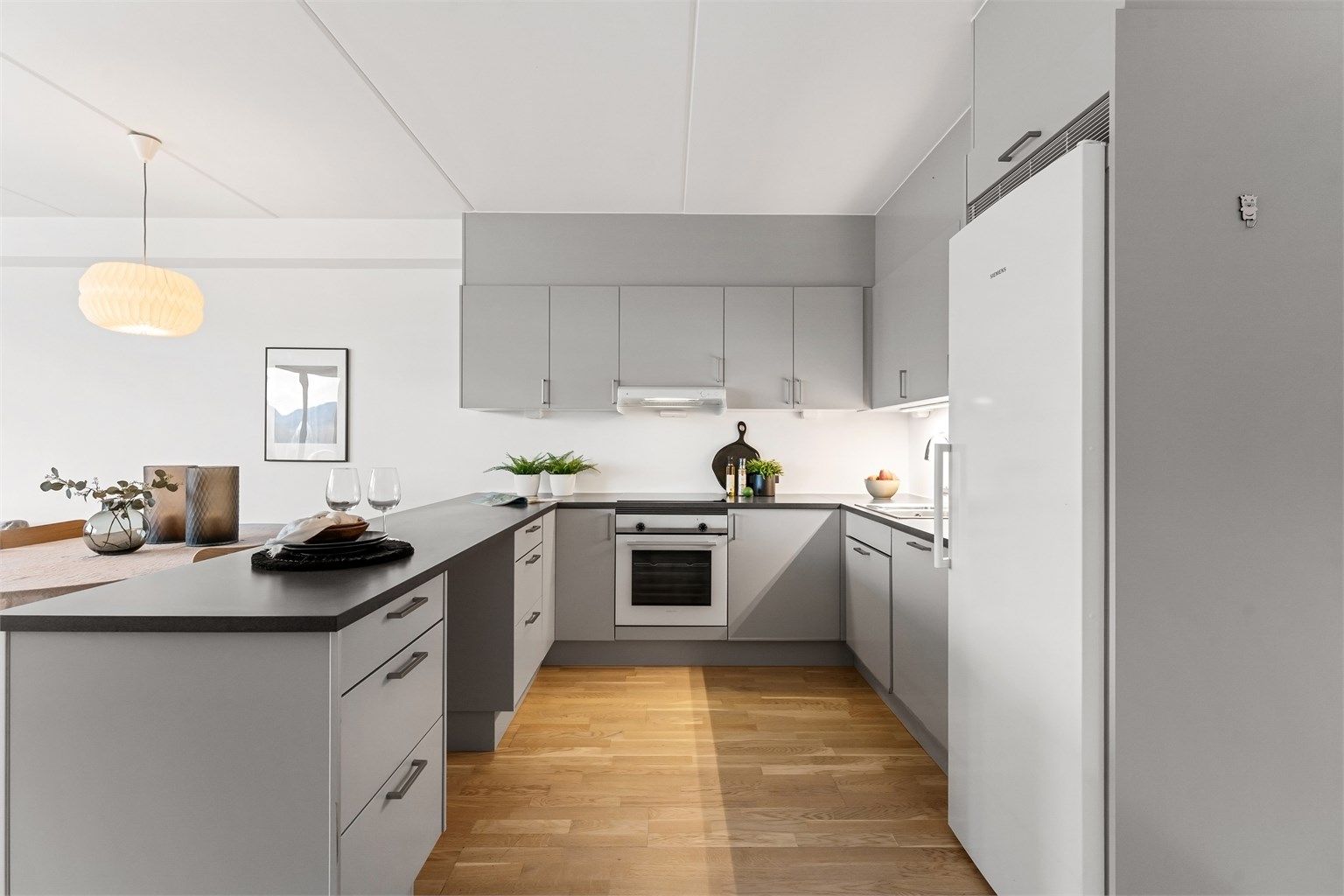 I åpen løsning finner du et delikat kjøkken med glatte fronter på skap og skuffer, og benkeplate i laminat med nedfelt kjøkkenvask