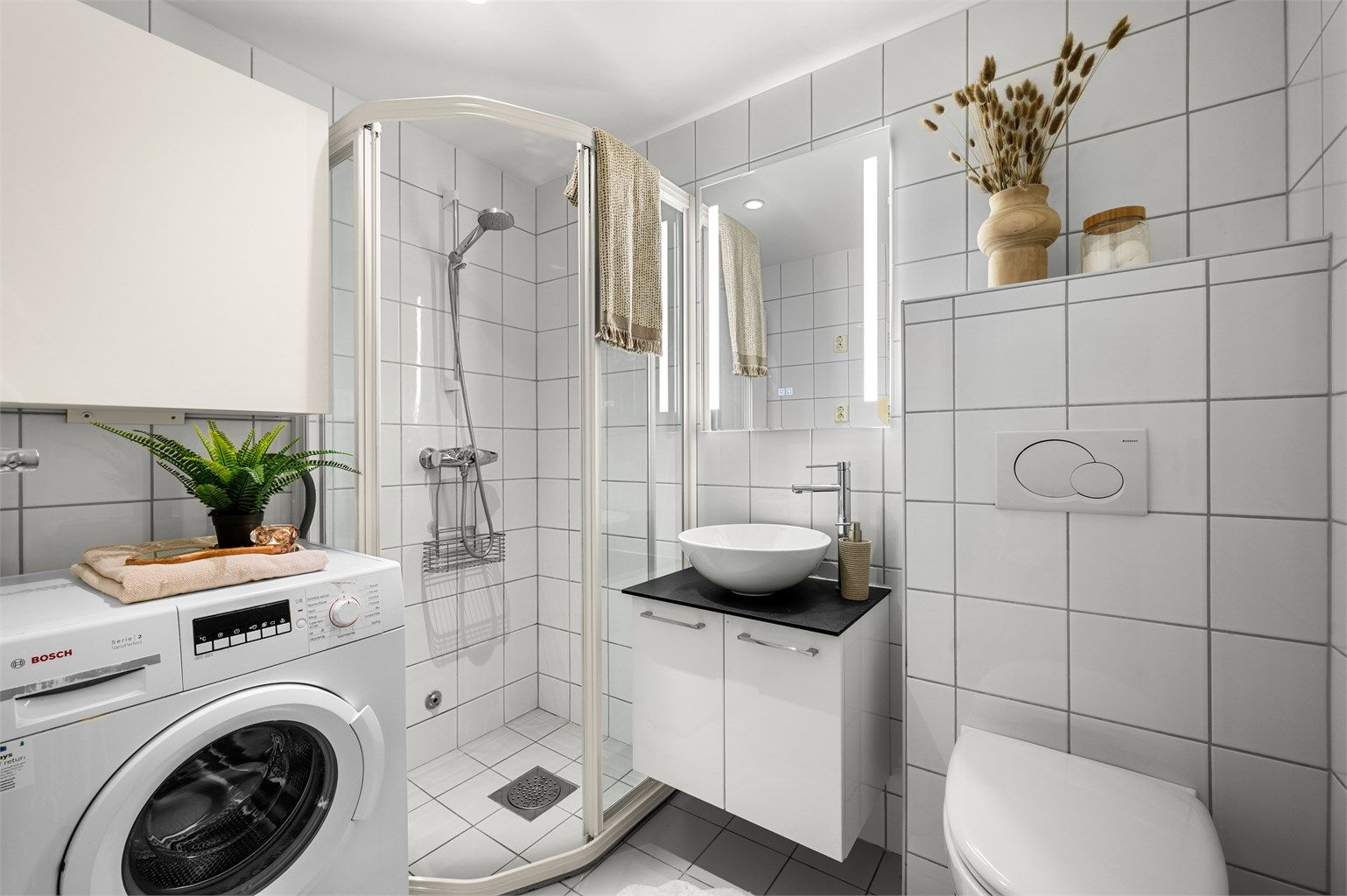 Pent flislagt bad med gulvvarme, downlights i himling og opplegg for vaskemaskin. Videre er badet innredet med servantskap med speil og lys, vegghengt toalett og dusjhjørne. 