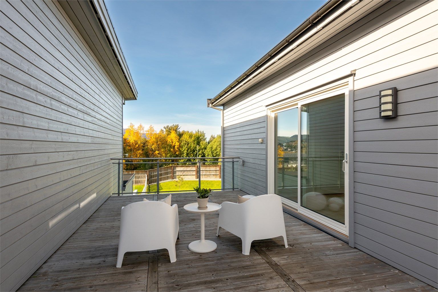 Romslig veranda i andre etasje med terrassebord og rekkverk i glass og metall.