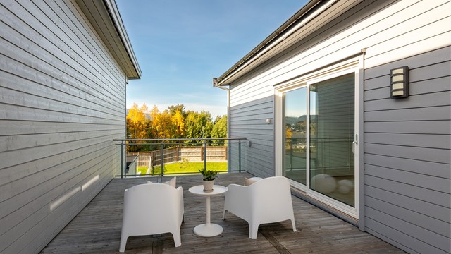 Romslig veranda i andre etasje med terrassebord og rekkverk i glass og metall.