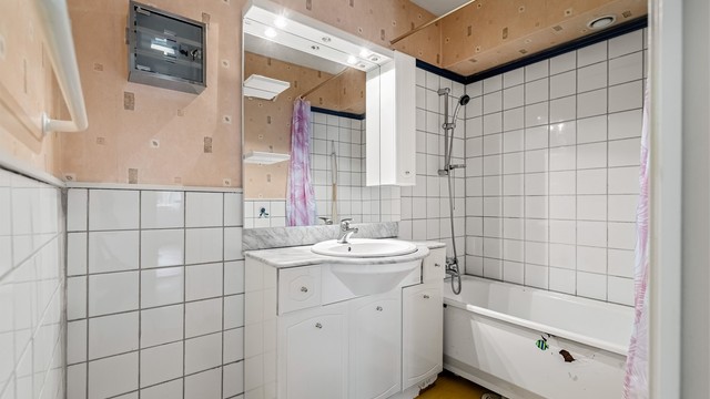 Baderom innredet med badekar, profilerte skapfronter, benkeplate i stein og nedsenket servant.