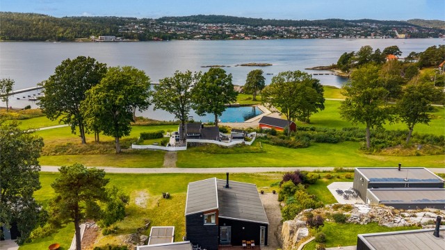 Den sortmalte funkishytta ligger åpent og fint i fremste rekke med utsikt utover sjøen.