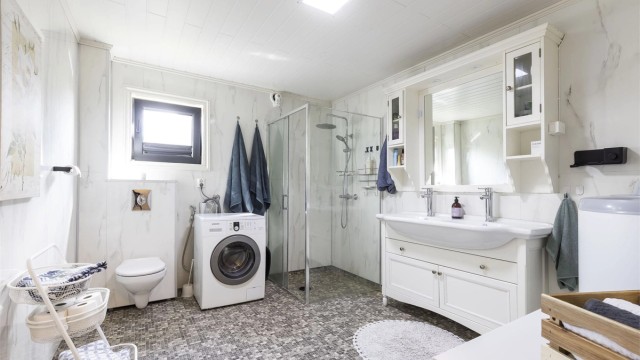 Bad fra 2021/2022. Gulv med belegg. Vegger med våtromsplater. Himling med mdf panel. Innredning med profilerte fronter. Heldekkende dobbelservant med overskap og speil.