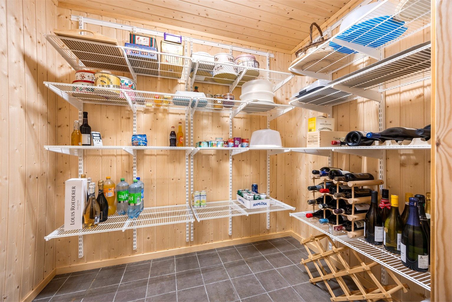 Plassbygd kjølerom i kjelleretasjen med faste vegghyller og kjøleaggregat.