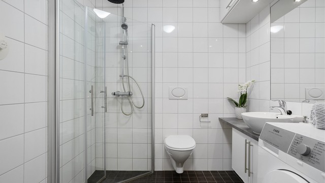 Flislagt bad med gulvvarme, vegghengt toalett og dusjhjørne med innfellbare glassdører.