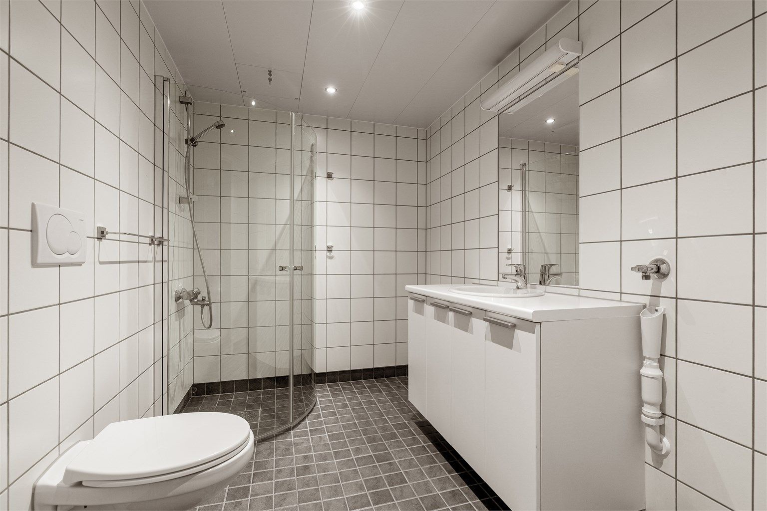 Flislagt bad med gulvvarme. Badet er innredet med vegghengt toalett, servantskap med speil og overlys, opplegg for vaskemaskin og tørketrommelm samt dusjhjørne
