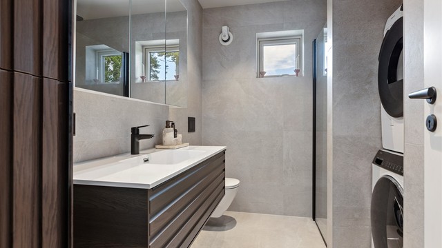 Badet har vegghengt toalett, dusjvegger og opplegg for vaskemaskin.