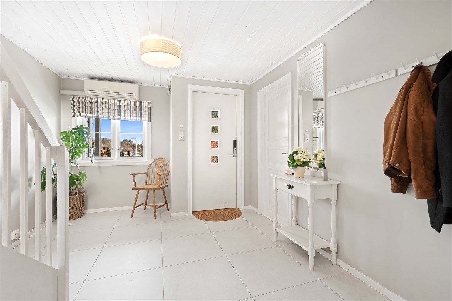 En lys og innbydende hall med varmepumpe og flislagt gulv og varmekabler.