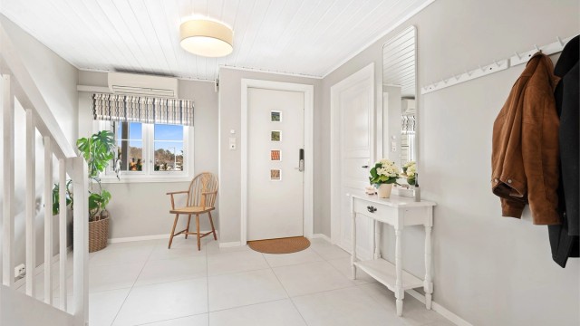 En lys og innbydende hall med varmepumpe og flislagt gulv og varmekabler.