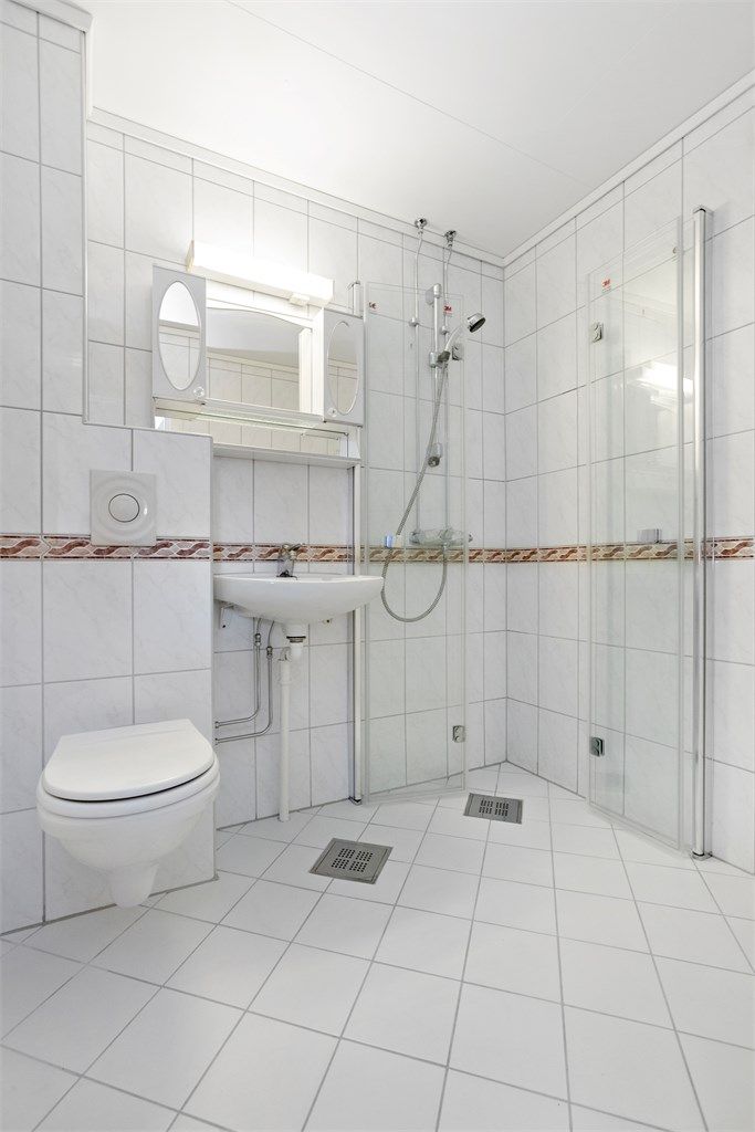 Flislagt bad med gulvvarme, vegghengt toalett og opplegg for vaskemaskin.