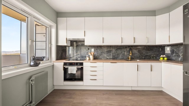 Stilrent kjøkken med glatte fronter, laminert benkeplate og fliser mellom benk og overskap.