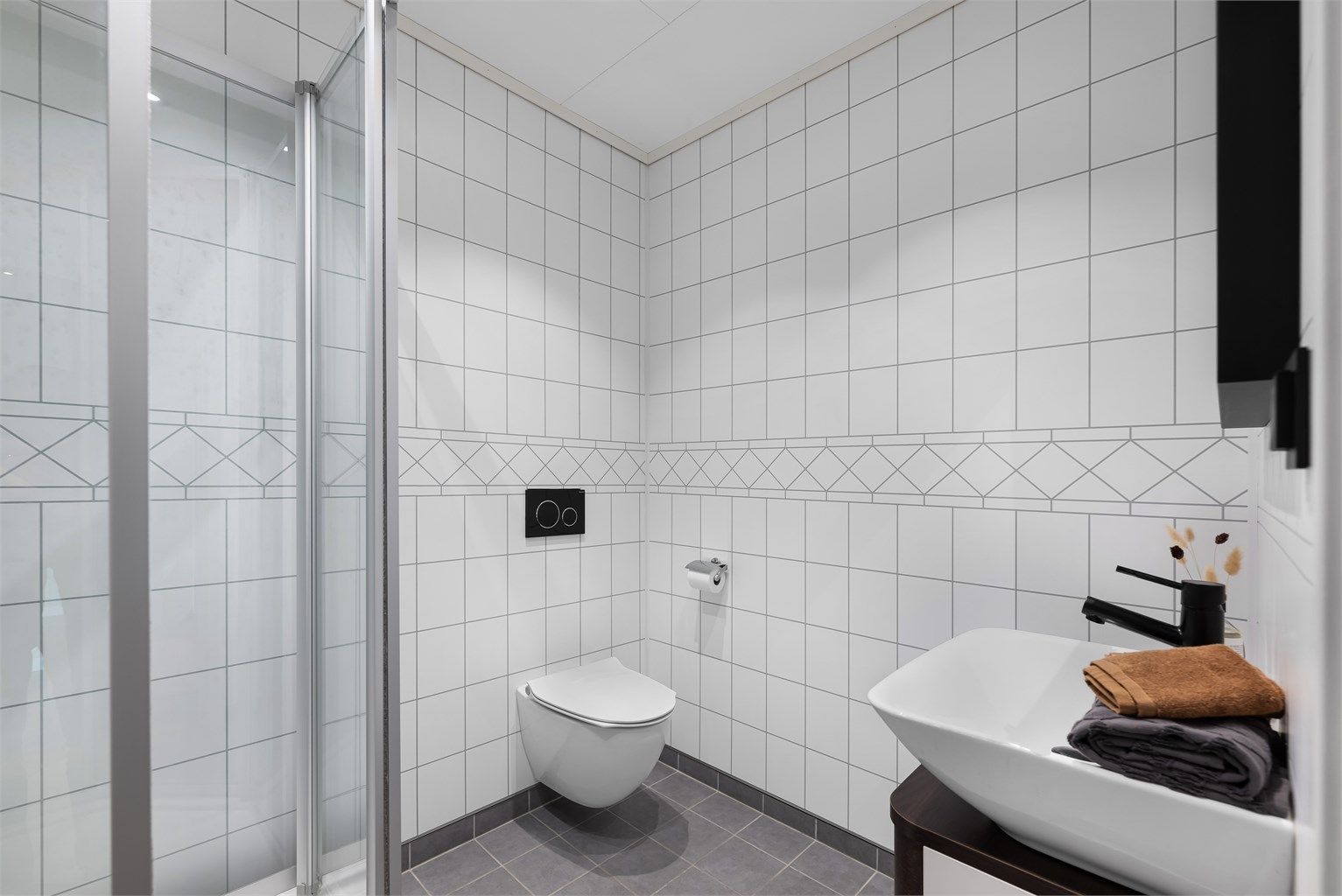 Moderne bad med fliser på gulv og plater på vegger, innredet med vegghengt wc, dusj og servant med baderomsinnredning