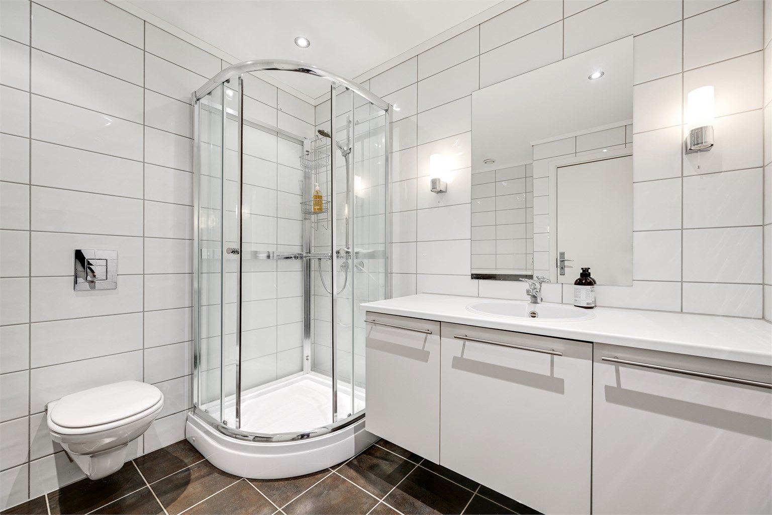 Badet er flislagt og utstyrt med toalett, servant i baderomsinnredning, dusjkabinett og opplegg for vaskemaskin.