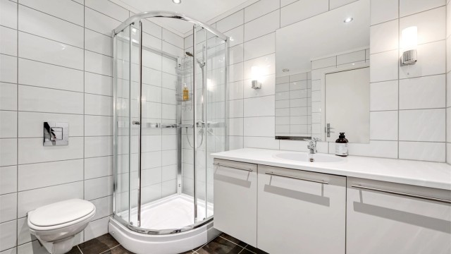 Badet er flislagt og utstyrt med toalett, servant i baderomsinnredning, dusjkabinett og opplegg for vaskemaskin.