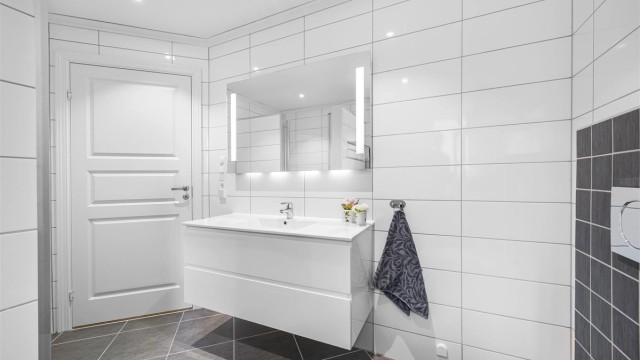 Baderomsinnredning med vegghengt servant, speil med belysning og downlights i taket.