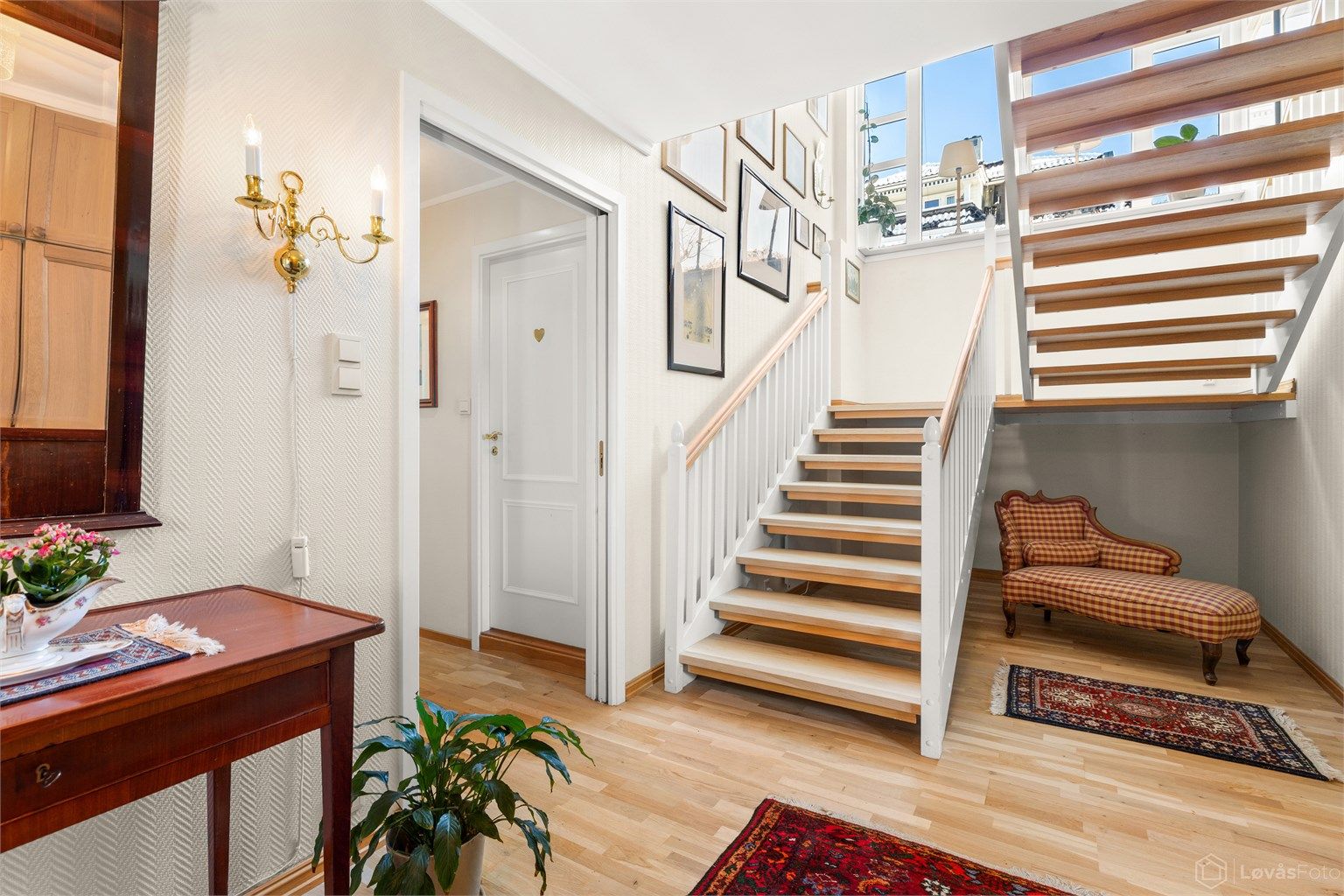 Romslig hall med garderobeskap. Store vindusflater i trappeløpet gir hallen godt med naturlig lys