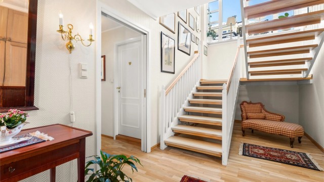 Romslig hall med garderobeskap. Store vindusflater i trappeløpet gir hallen godt med naturlig lys