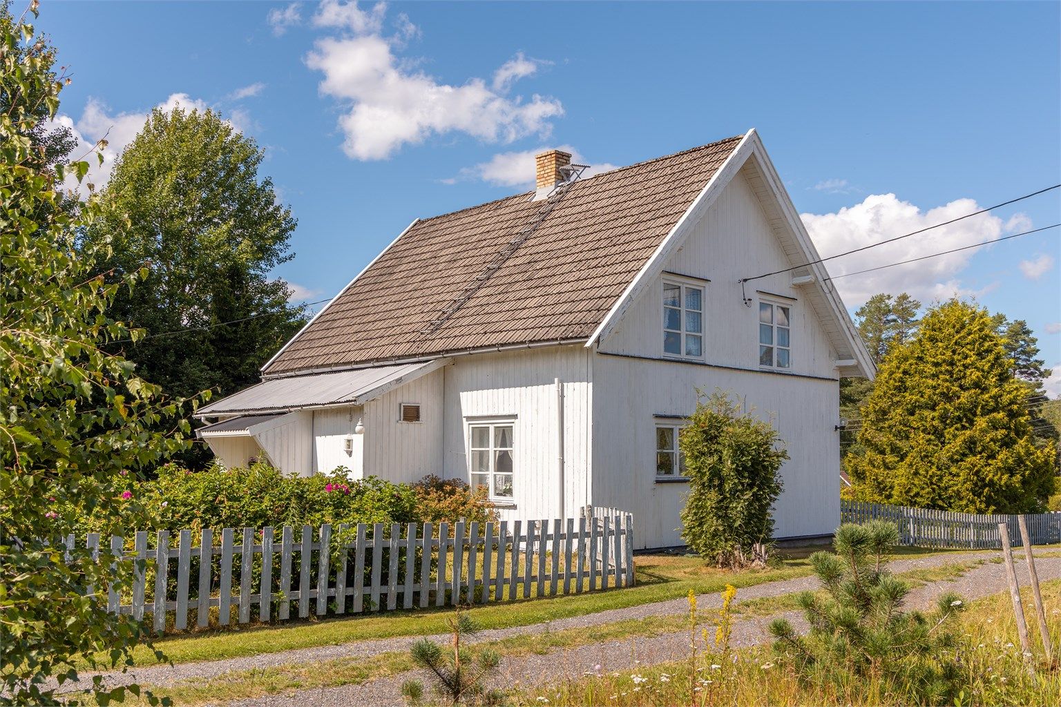 Huset er omgitt av en hage og hvit stakittgjerde som gir en skjermet og privat følelse.