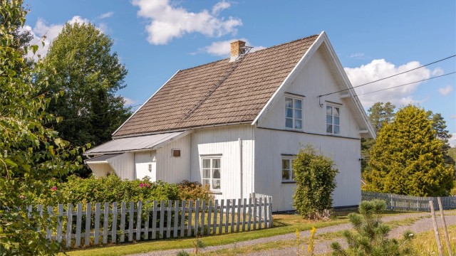 Huset er omgitt av en hage og hvit stakittgjerde som gir en skjermet og privat følelse.