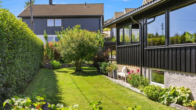 Den velholdte hagen er pent opparbeidet med plen og beplantning som skaper et grønt og innbydende utemiljø.