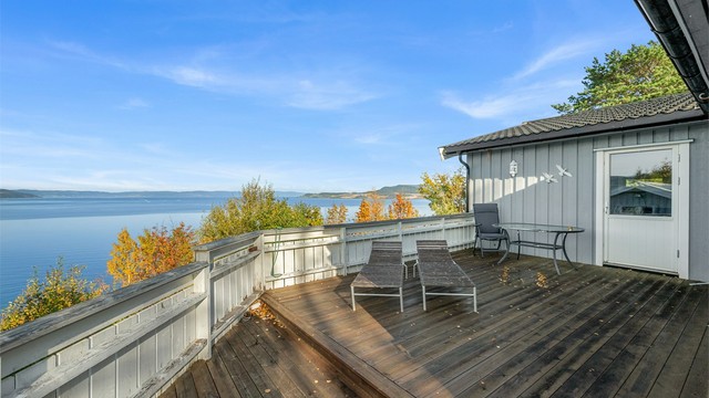 Balkong og terrasse i trekonstruksjoner med rekkverk og åpen utsikt mot fjorden.