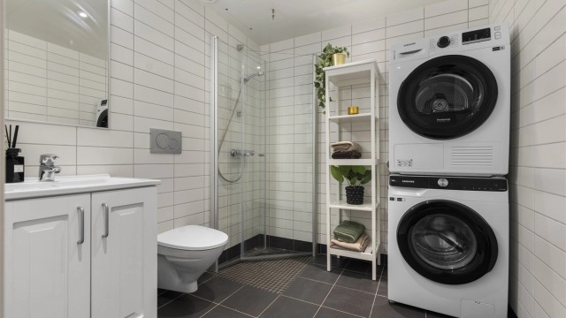 Flislagt og moderne baderom med vegghengt toalett og dusjhjørne.