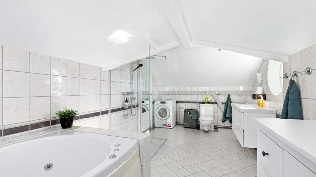 Baderommet er innredet med dusj med glassvegger, separat badekar og opplegg for vaskemaskin.