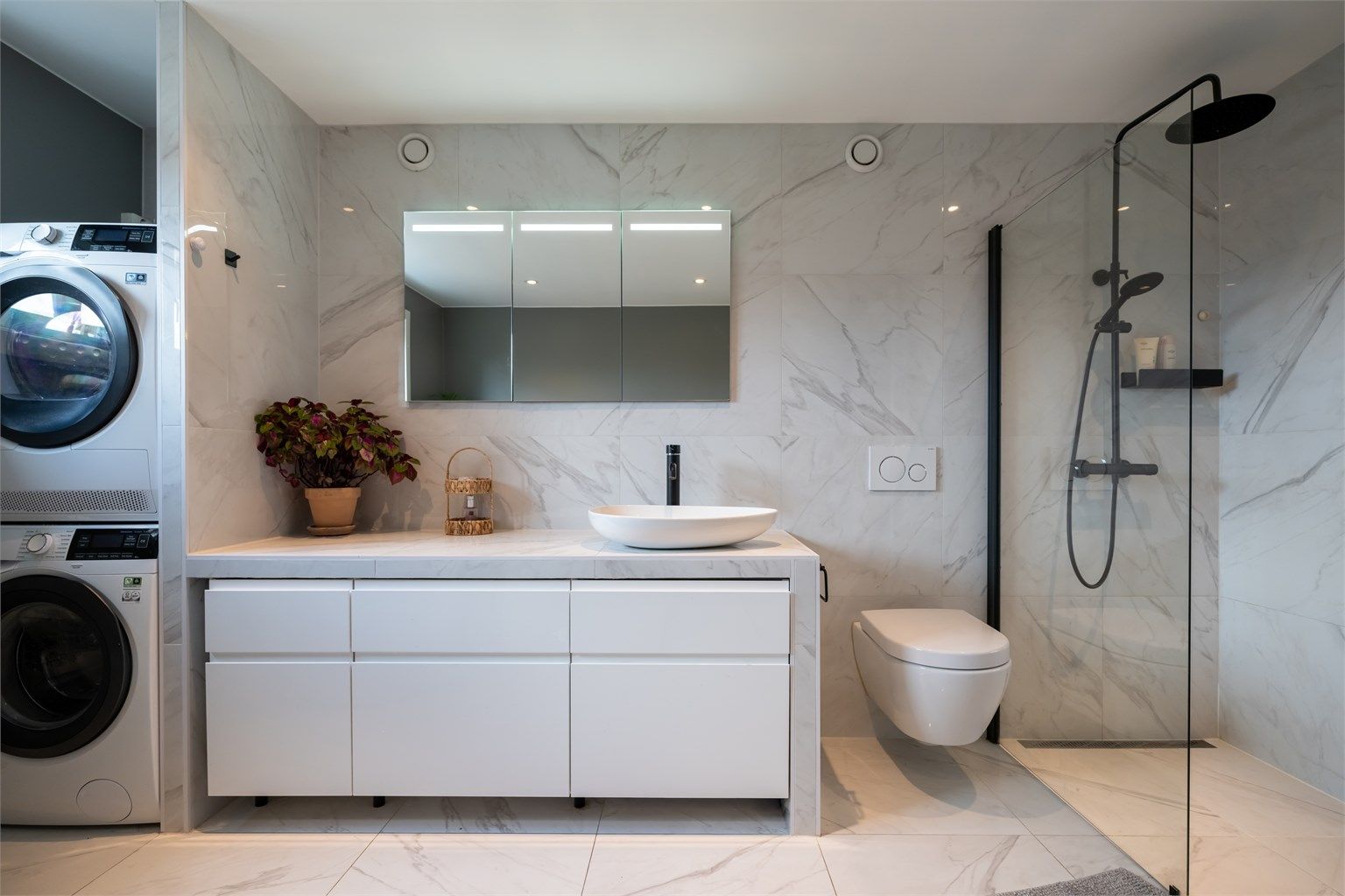 Badet er innredet med servantskap med ovenpåliggende vask, speil med belysning over servant og vegghengt toalett.