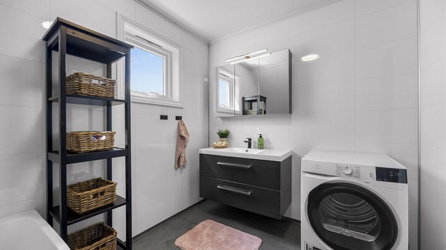 Badet har baderomsplater på veggene og vinylbelegg på gulvet.