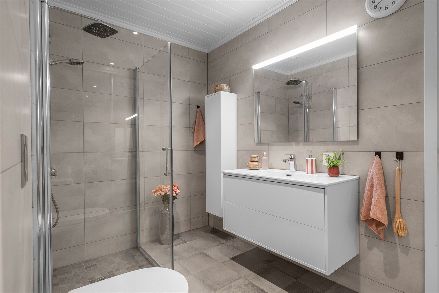 Badet er fra byggeår og har flislagt gulv med gulvvarme samt flislagte vegger.  Innredningen består av vegghengt servantinnredning med ovenpåliggende servant og armatur, speil med overlys og stikkontakt samt vegghengt høyskap.