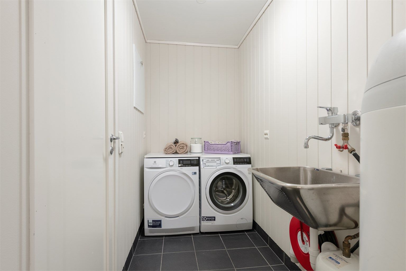 Praktisk vaskerom i underetasjen med flislagt gulv med gulvvarme, utslagsvask og opplegg for vaskemaskin.