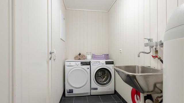 Praktisk vaskerom i underetasjen med flislagt gulv med gulvvarme, utslagsvask og opplegg for vaskemaskin.