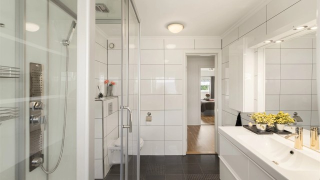 Badet er innredet med dusjkabinett, vegghengt toalett og servant i innredning