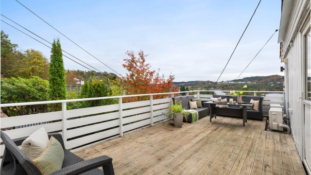 Romslig balkong belagt med terrassebord og hvitmalt rekkverk.