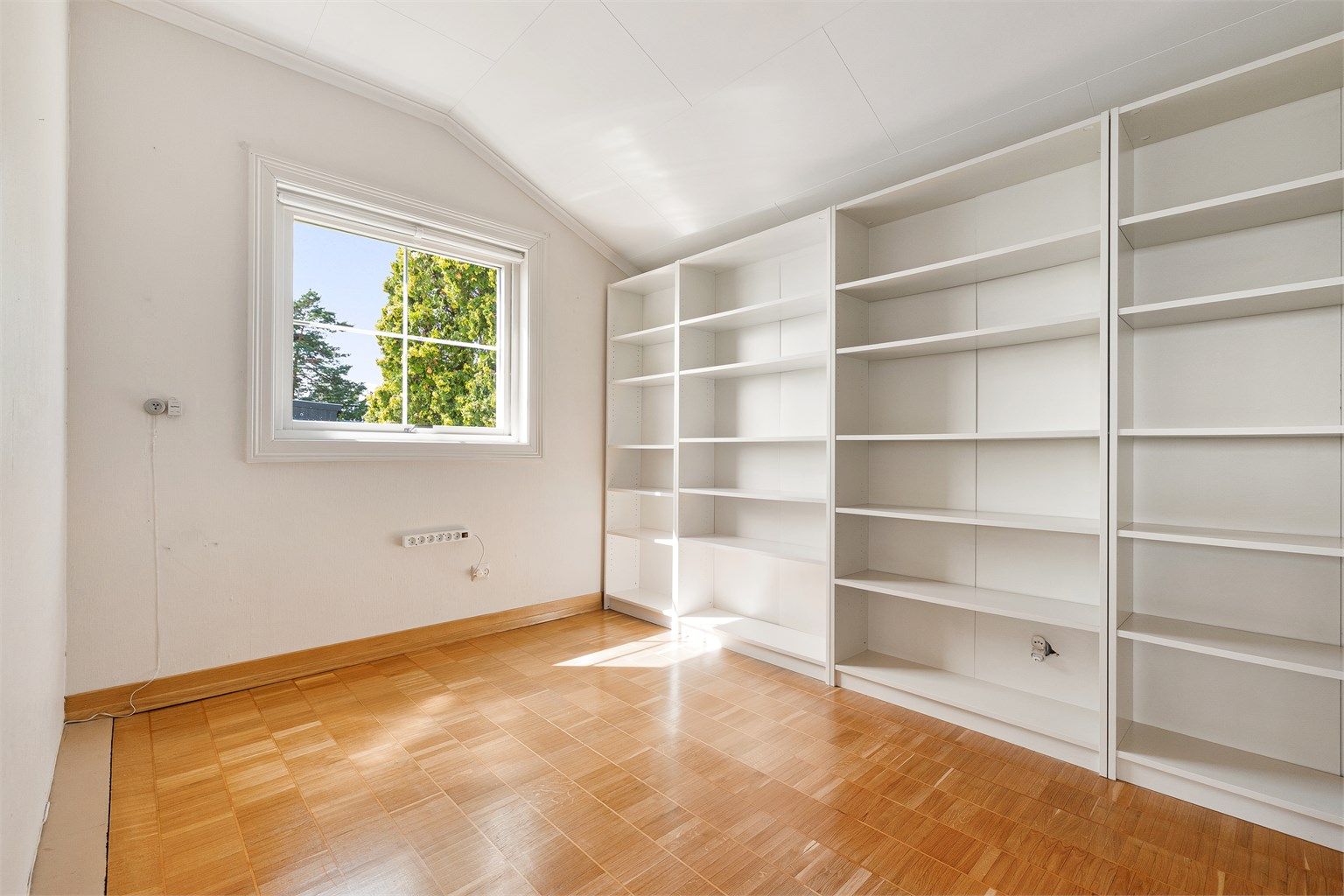 Etasjen har ett soverom med skråtak langs den ene veggen. En vegg med innebygde hyller gir gode oppbevaringsmuligheter, og vinduet vender mot hagen.